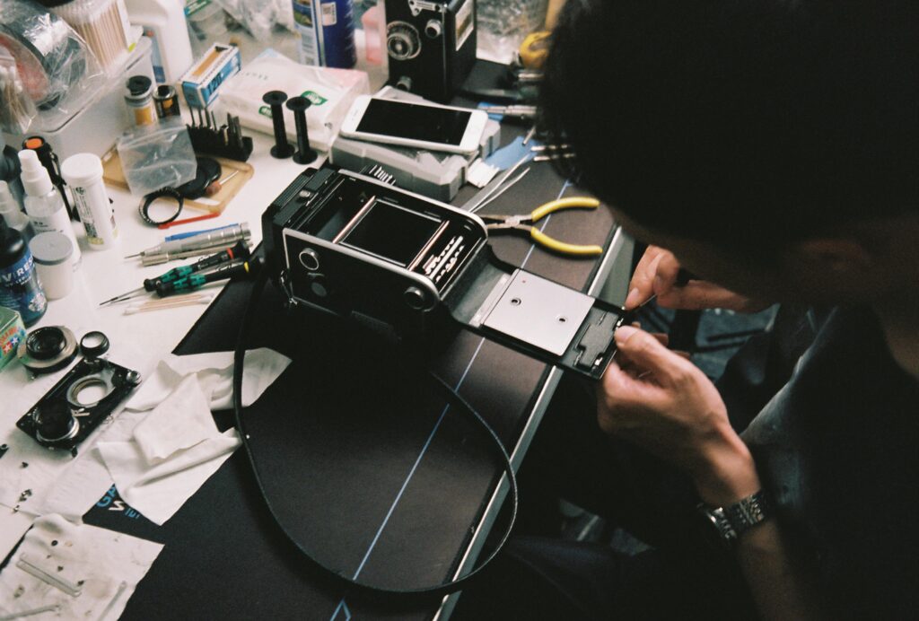 A man skillfully repairs a vintage camera in a cluttered workshop filled with tools.