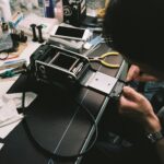 A man skillfully repairs a vintage camera in a cluttered workshop filled with tools.